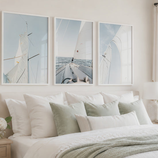 A bright coastal bedroom showcases three blue sailboat prints in white frames as the camera gently moves closer