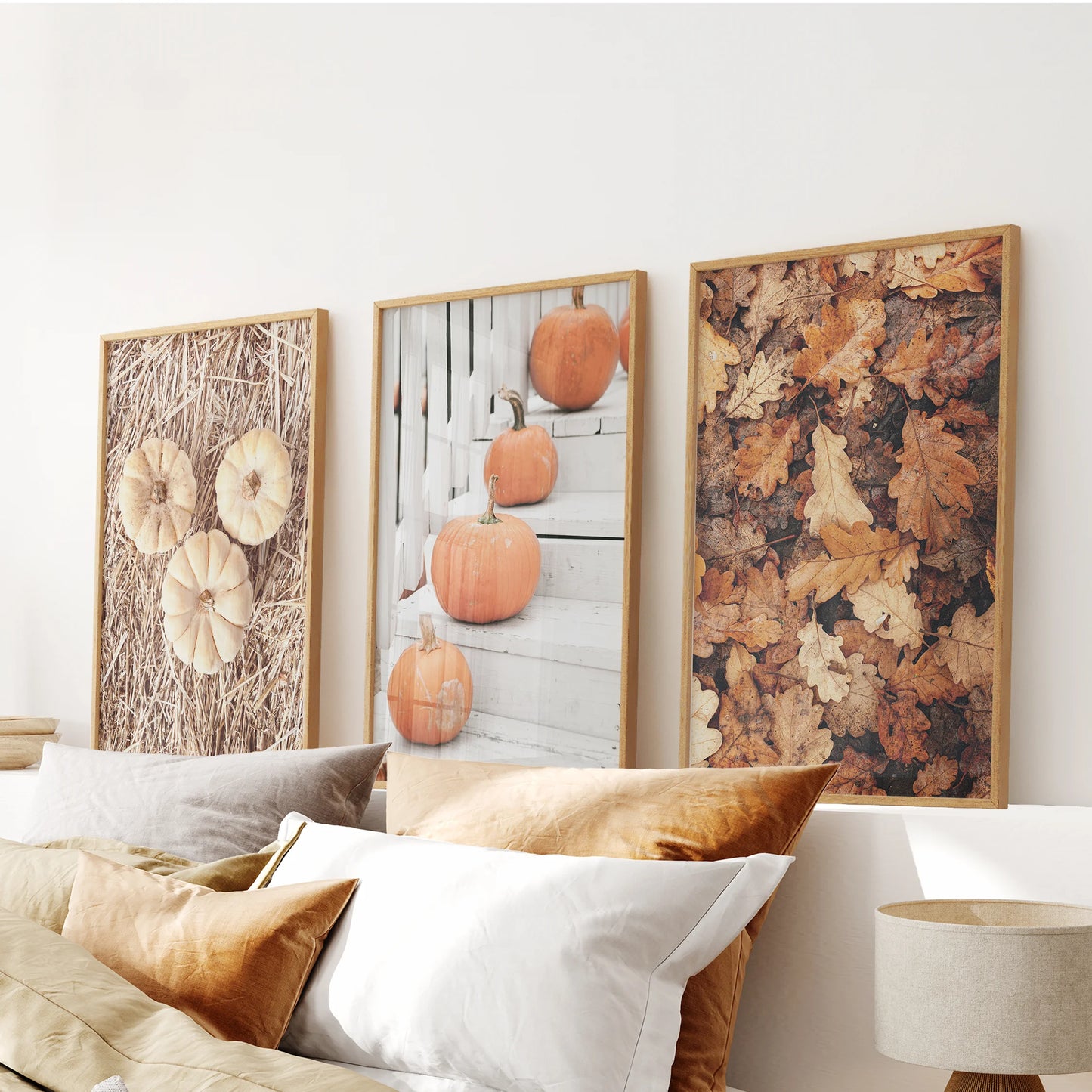 Three autumn art prints in thin wood frames hang above the bed, layering rustic gourds and leaves with gentle harvest color.