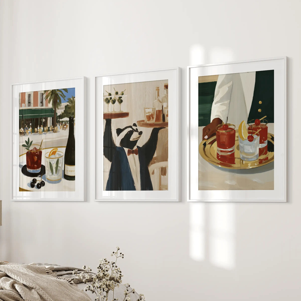 Cocktail drinks in a three-piece wall art set, presented in white matted frames on the bedroom wall beside the bed.