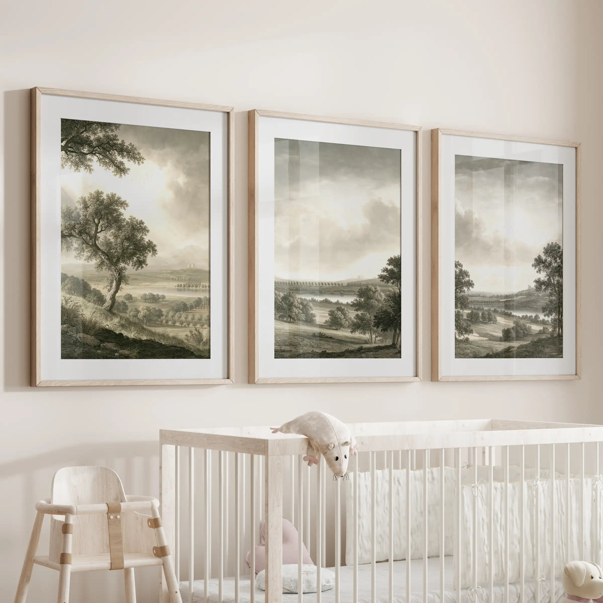 Pastoral landscape wall art in a set of three, with matted prints in thin wood frames above a cot in a baby nursery.