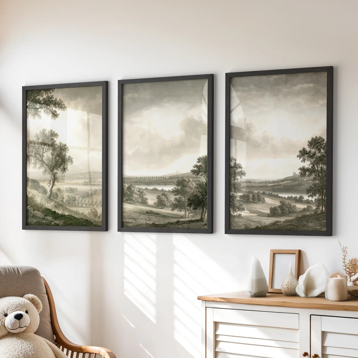 Pastoral landscape wall art in a set of three, shown as black-framed prints above a chest of drawers in a kids room.