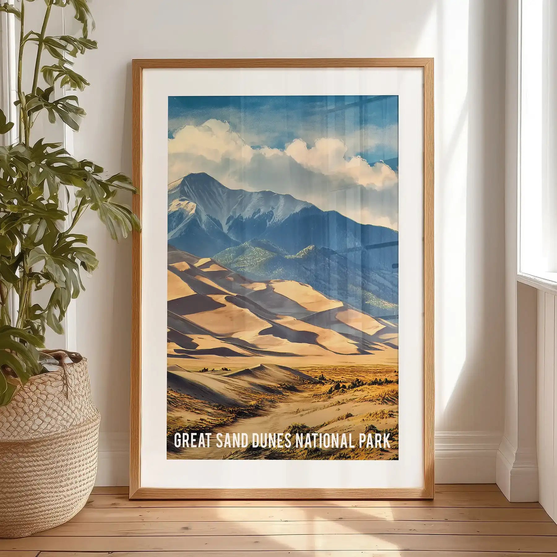 A black-matted framed print of the San Luis Valley’s dunes and mountains stands near a bedroom window, casting warm desert tones through the light.