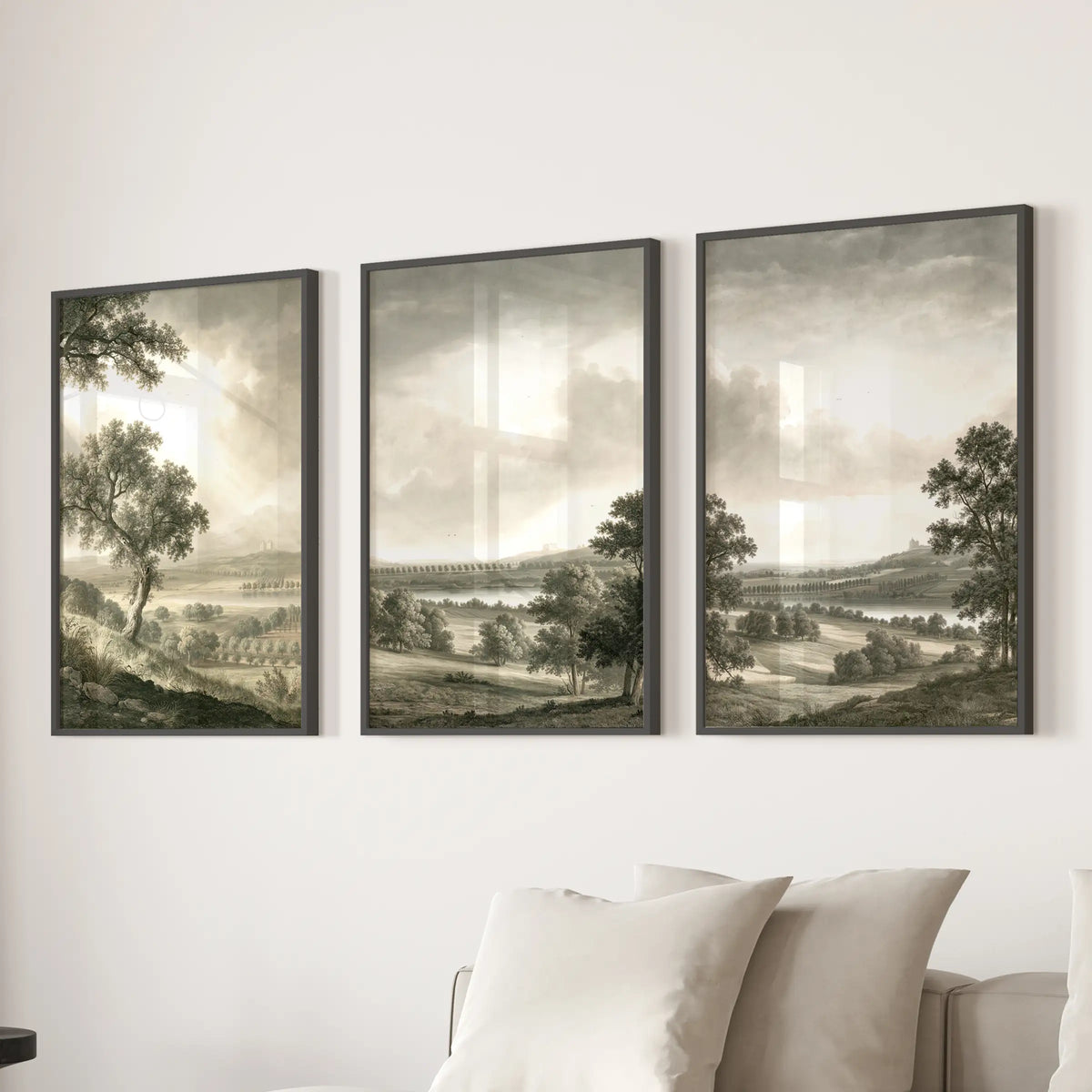Countryside scenery three-piece wall art set in black frames, displayed behind a sofa in a sitting room.