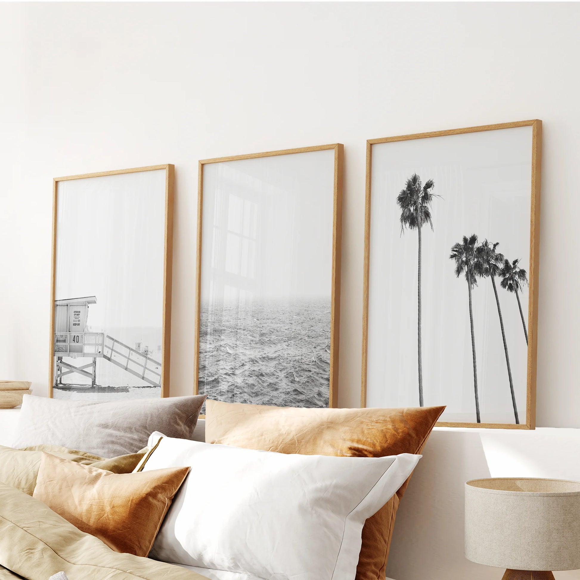 Black-and-white beach scenes, a three-piece wall decor set in light oak frames, anchor the bedroom above the headboard with warm, surf-washed minimalism.