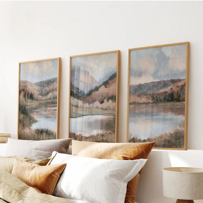 A three-print gallery wall of moody hills above a calm lake, held in warm wooden frames, hangs over the bedroom headboard for a restful, mist-washed look.