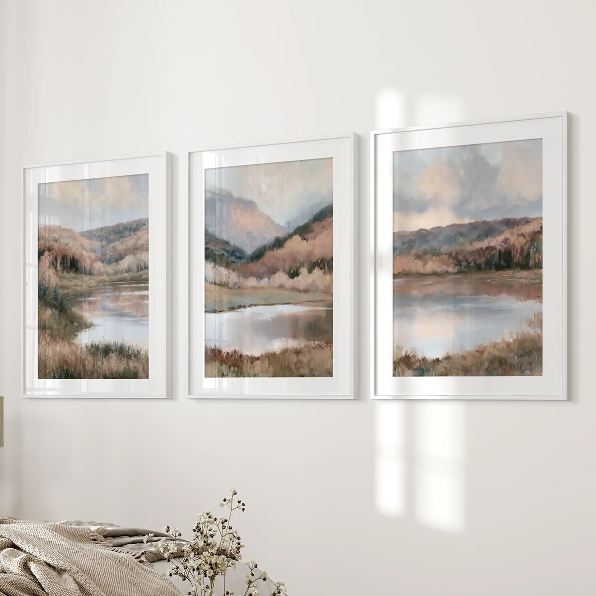 Water reflections with shoreline trees, a print set of three in white frames with mats, frames the wall next to the bed in the bedroom with tranquil, airy scenery.