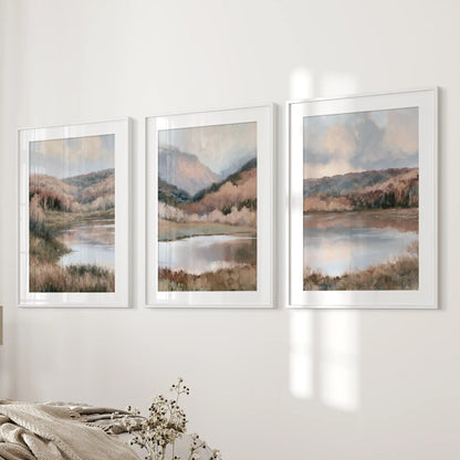 Water reflections with shoreline trees, a print set of three in white frames with mats, frames the wall next to the bed in the bedroom with tranquil, airy scenery.