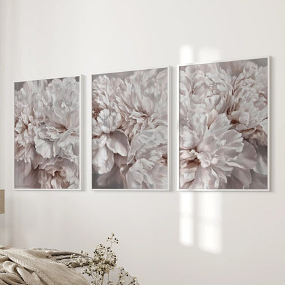Layers of blush and ivory petals overlap in three white-framed prints beside a bed, with soft shadows between the ruffled edges.