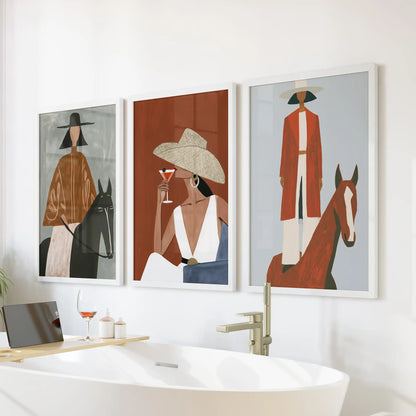 A three-piece wall print set of cowgirl portraits in crisp white frames brightens the bathroom wall above the bathtub with calm western charm.
