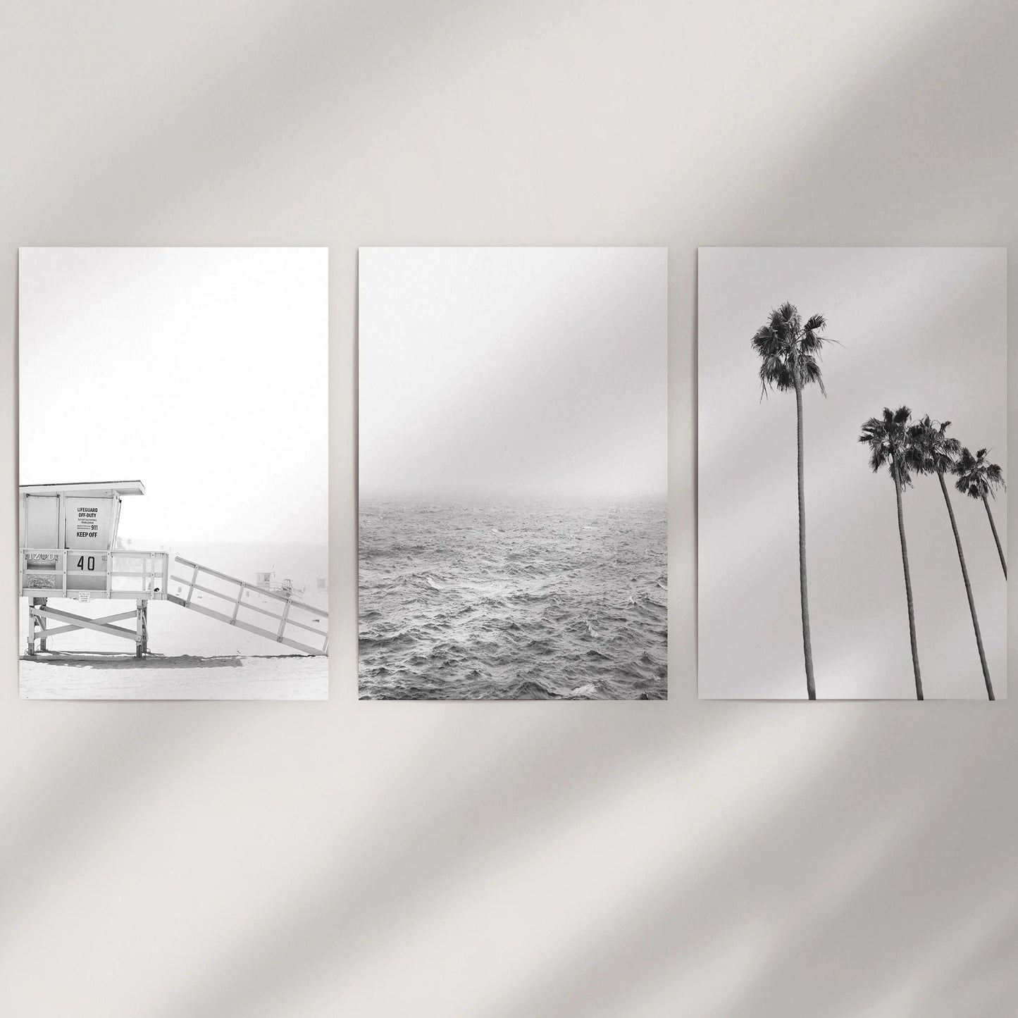A set of three rolled art prints with black-and-white beach scenes waits to be displayed on a blank wall as a modern coastal trio.