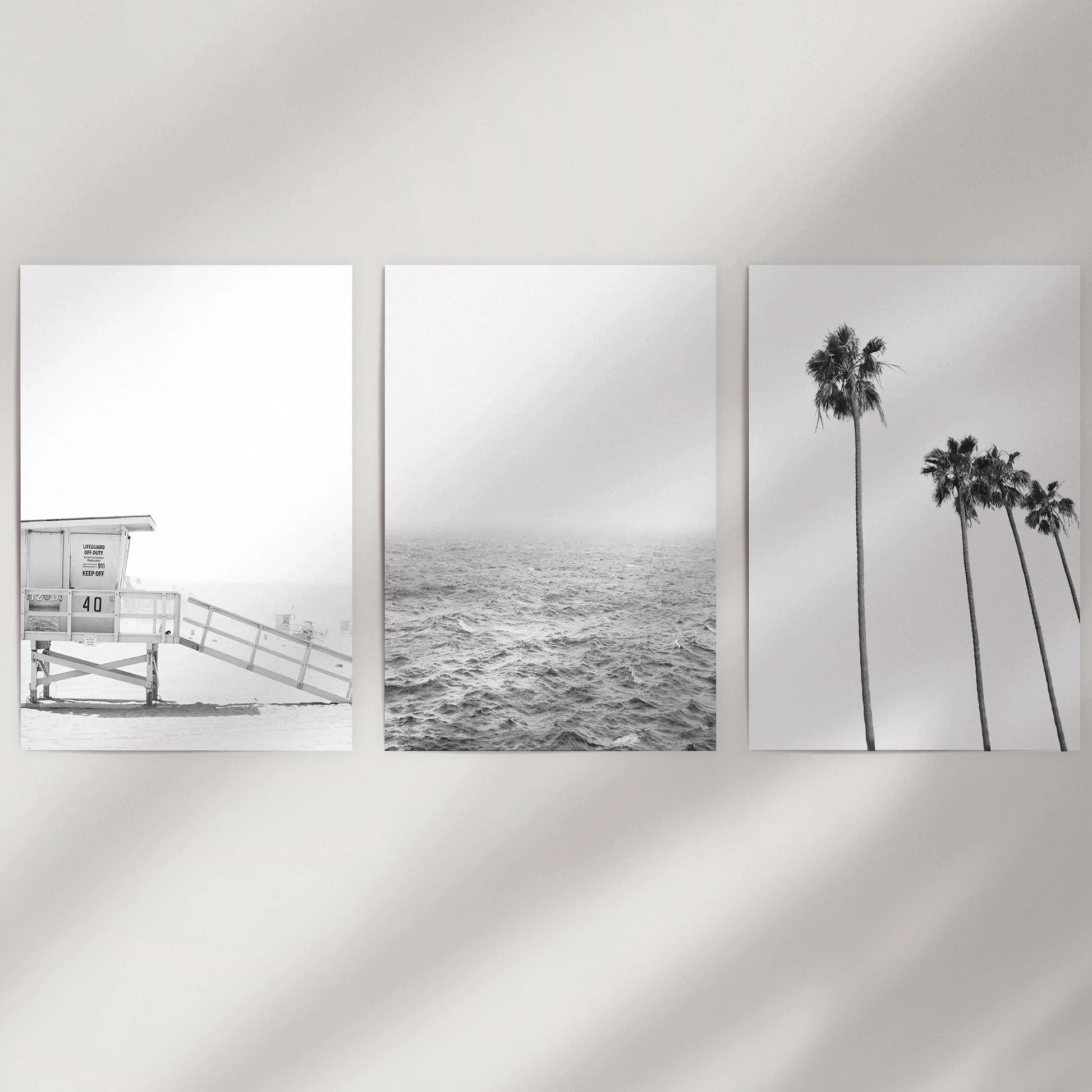 A set of three rolled art prints with black-and-white beach scenes waits to be displayed on a blank wall as a modern coastal trio.