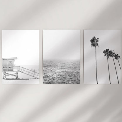 A set of three rolled art prints with black-and-white beach scenes waits to be displayed on a blank wall as a modern coastal trio.