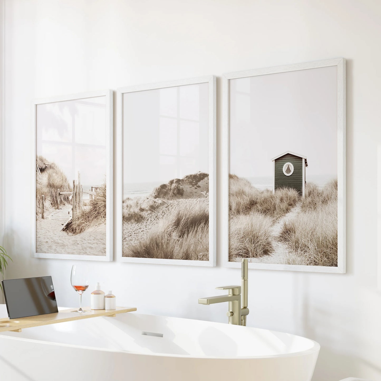 A white-framed coastal trio hangs over the bathtub wall, soft dunes and pastel sky giving the bathroom a spa-like, serene feel.