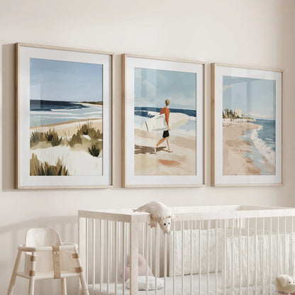 Coastal beach scenes, a three-print gallery wall in thin wood frames with mats, settles above the cot and keeps the nursery airy and calm.