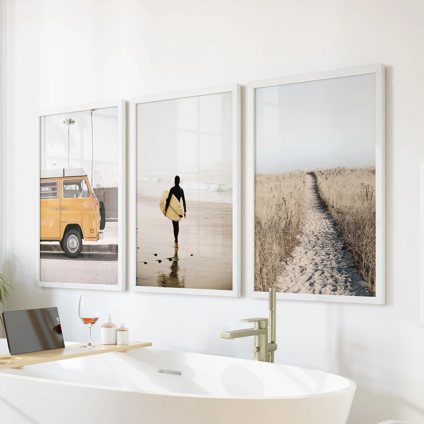 Gallery wall of three surfer-wave prints in white frames sits above the soaking tub, adding breezy motion to a calm bathroom scene.