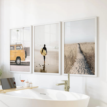 Gallery wall of three surfer-wave prints in white frames sits above the soaking tub, adding breezy motion to a calm bathroom scene.
