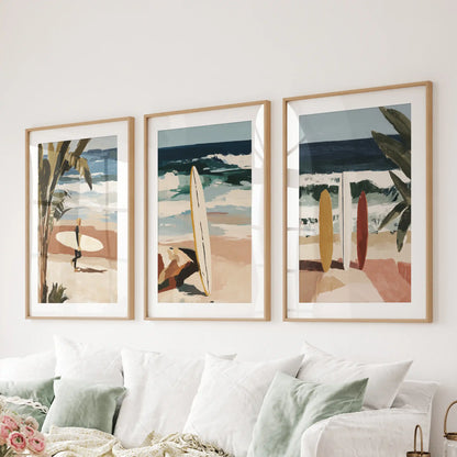 Surfers set of 3 posters in oak frames with mats hangs behind the living-room couch, capturing silhouettes carving across golden late-day swells.