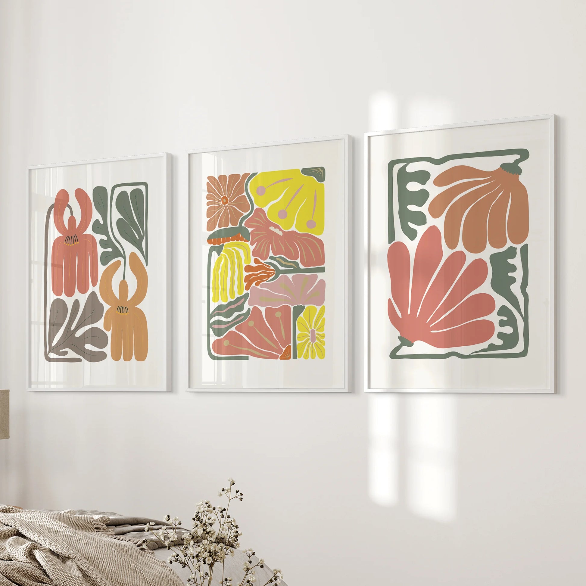Terracotta floral artwork in a three-piece wall set rests near the bedroom’s bed wall, cleanly framed in white to pop the warm botanicals against soft linens.