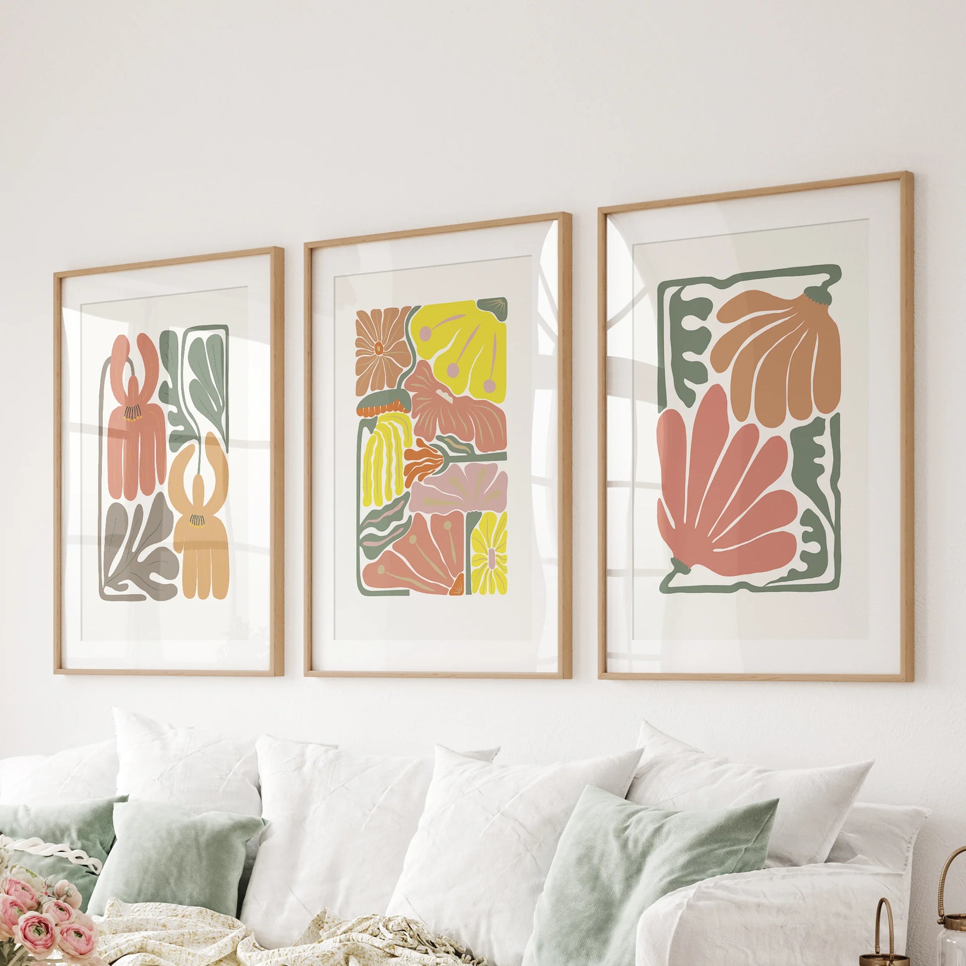 Behind the lounge sofa, a wall set of three terracotta floral prints sits in matted natural wood frames, highlighting earthy color and calm form.