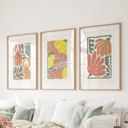 Behind the lounge sofa, a wall set of three terracotta floral prints sits in matted natural wood frames, highlighting earthy color and calm form.