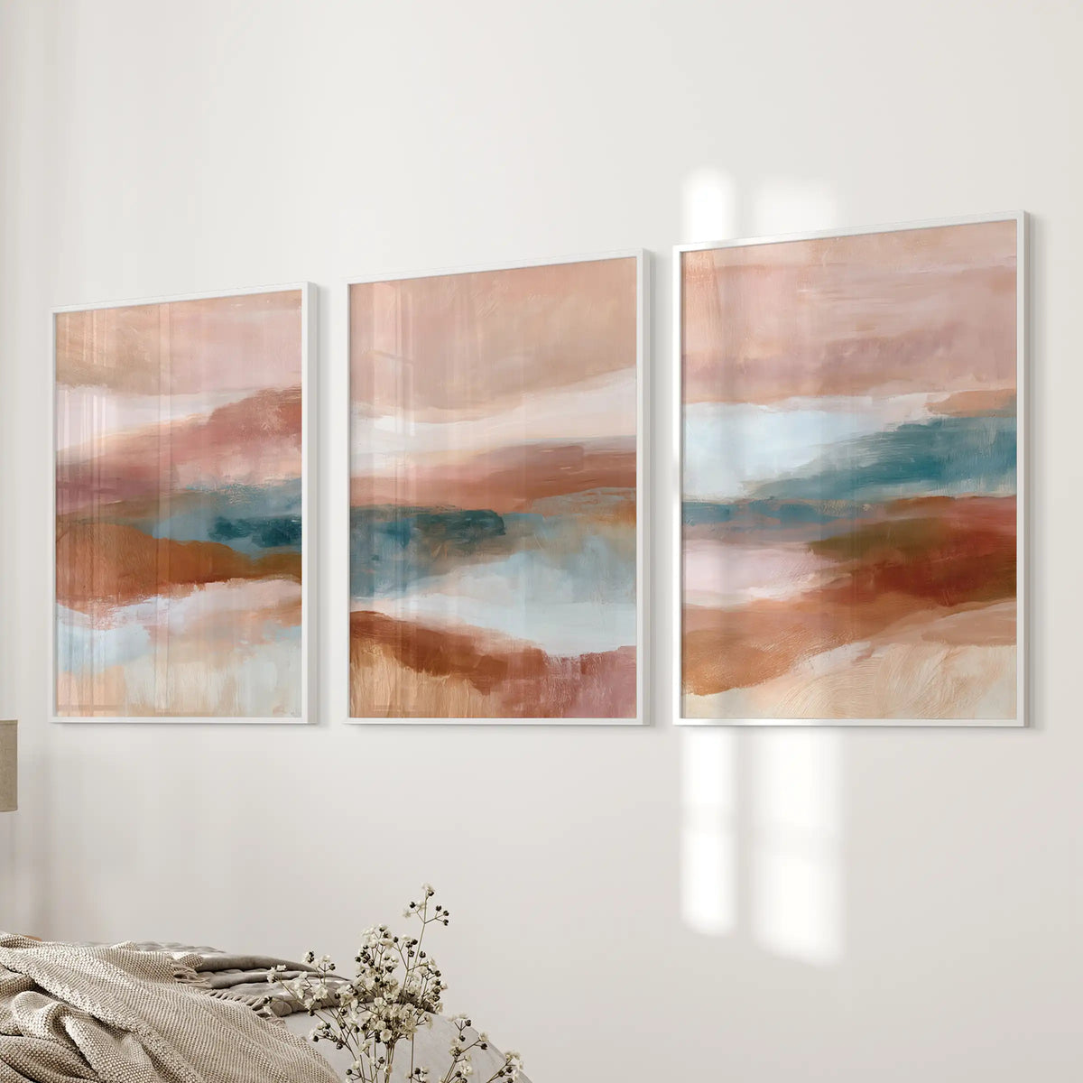 Blush pink, terracotta and blue color fields, three white-framed art prints, line the bedroom wall next to the bed with soft contrast.
