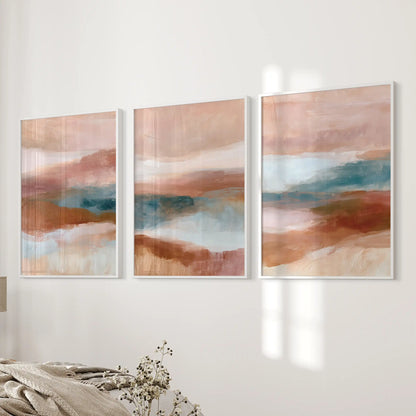 Blush pink, terracotta and blue color fields, three white-framed art prints, line the bedroom wall next to the bed with soft contrast.