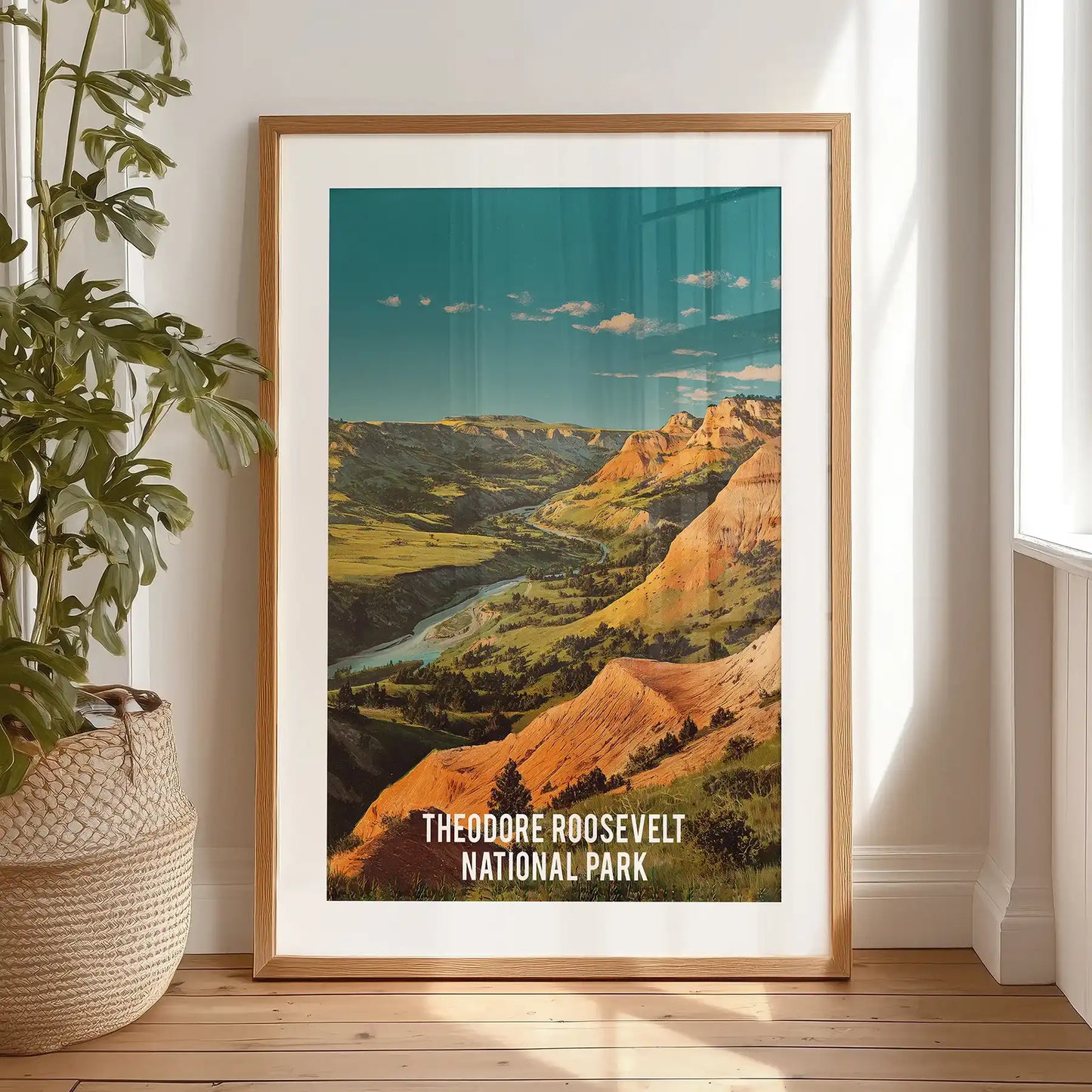 Single poster print of the Little Missouri River canyon rests on the bedroom floor before hanging, framed cleanly with a black mat.