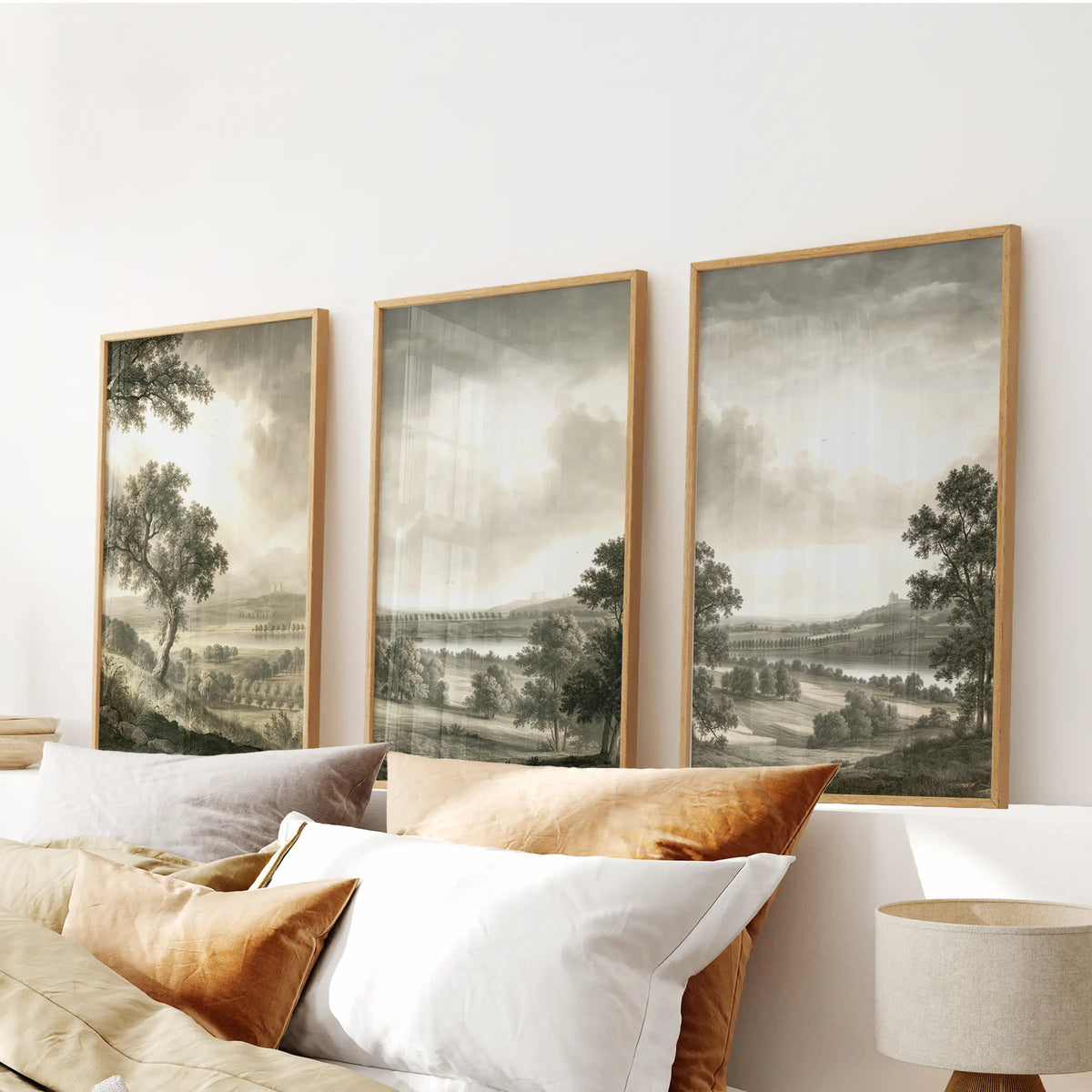 Trees and fields wall art in a three-piece hanging, with thin wood-framed prints displayed above the headboard in a bedroom.