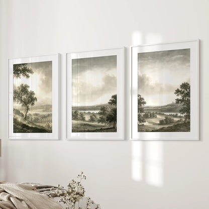 Rural landscape wall art in three pieces, shown in white matted frames on the wall next to a bed in a bedroom.