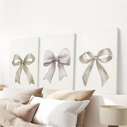 Three gallery-wrapped ribbon canvases spread across the wall above the bedroom headboard, their creamy bows adding subtle texture and calm.