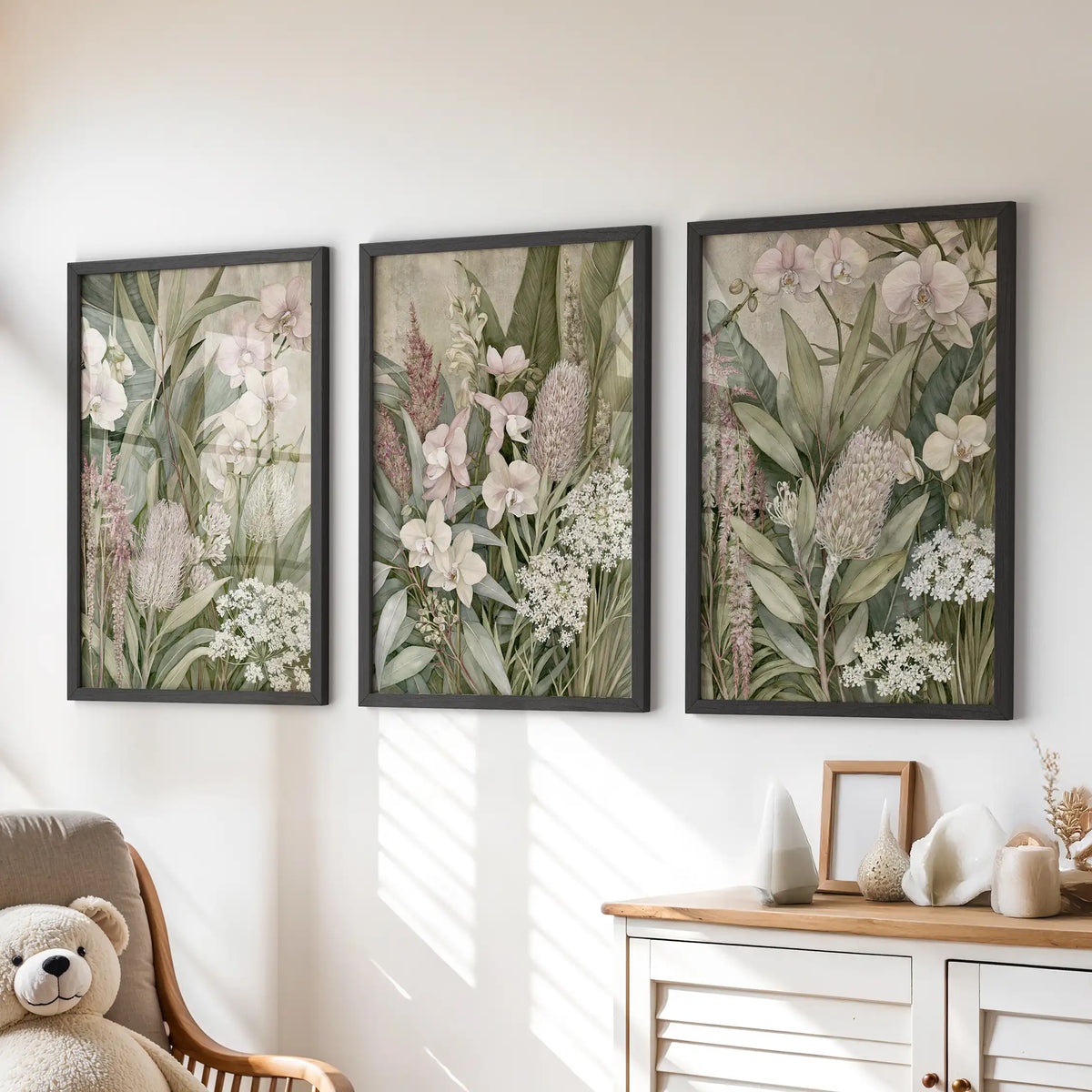 Pale orchids and upright green leaves appear above a dresser in three black-framed prints, with mottled beige behind the layered plants.