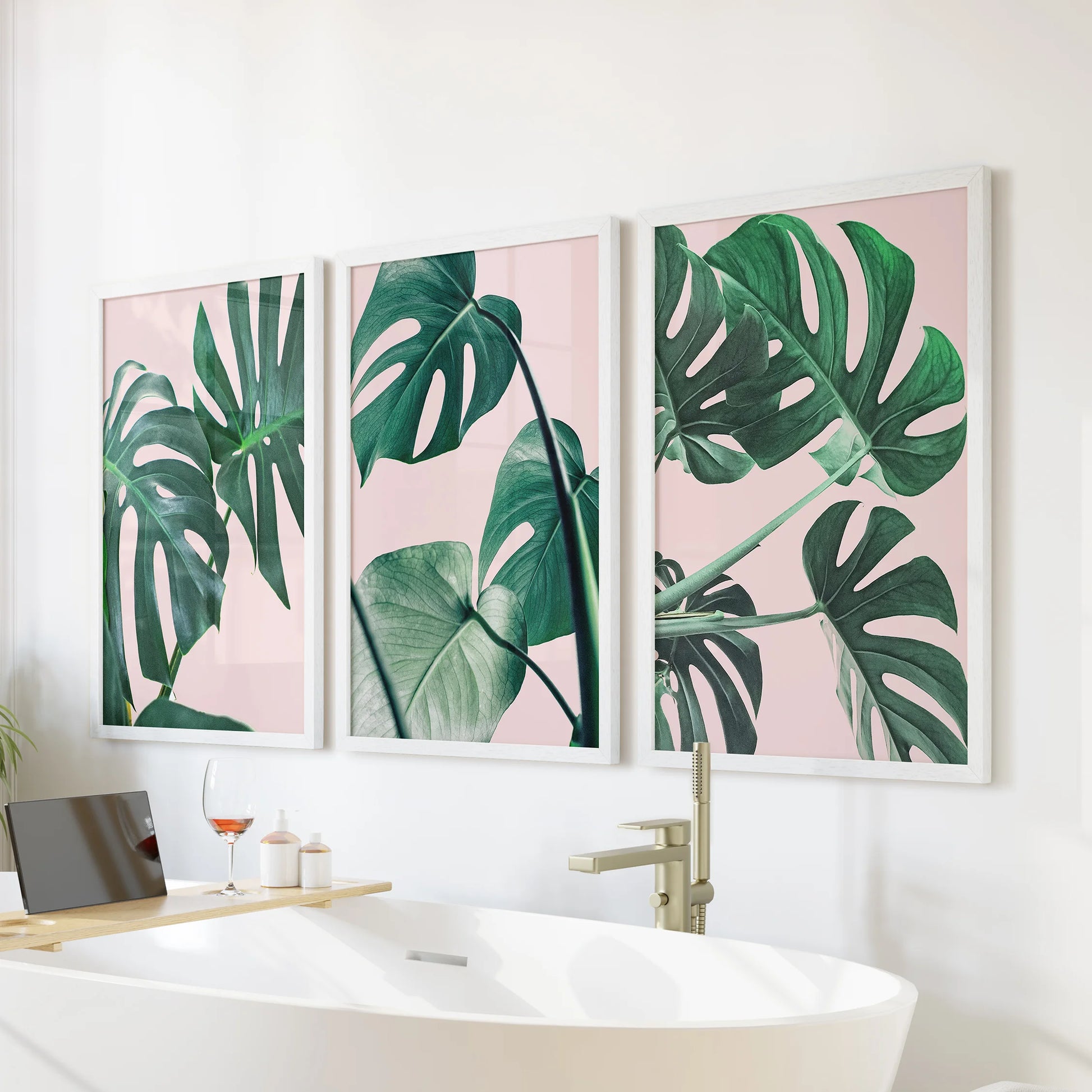 Pink monstera leaves wall art, a white-framed three-piece set, lines the space above the bathtub to bring spa-light tropical calm to the bathroom.