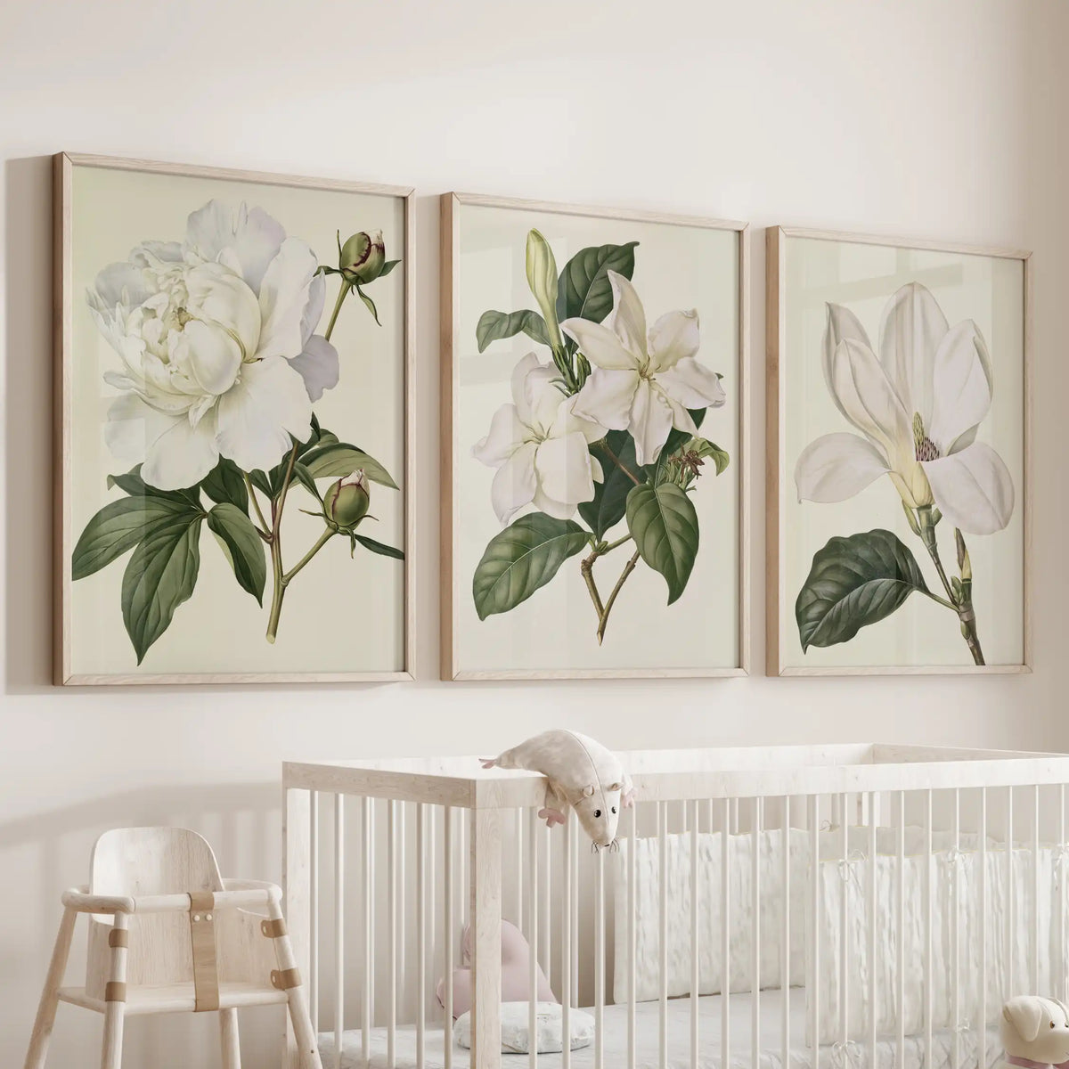 A ruffled white bloom sits beside two other flowering stems in three oak-framed prints above a crib, all on cream backgrounds.