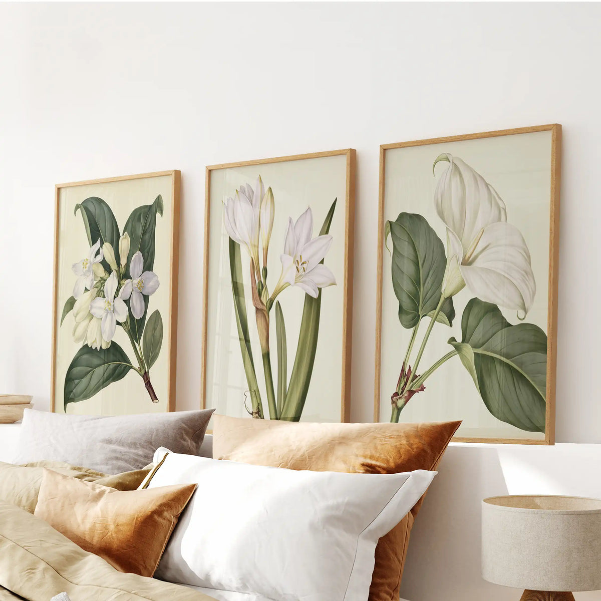 White botanical flowers fill three oak-framed prints above a bed.
