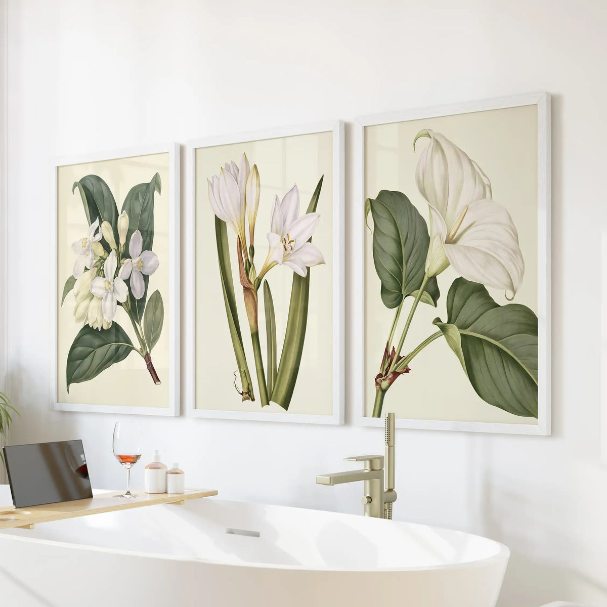 White frames display small blossoms, long upright stems and a large white flower with broad leaves across three prints above a bathtub.
