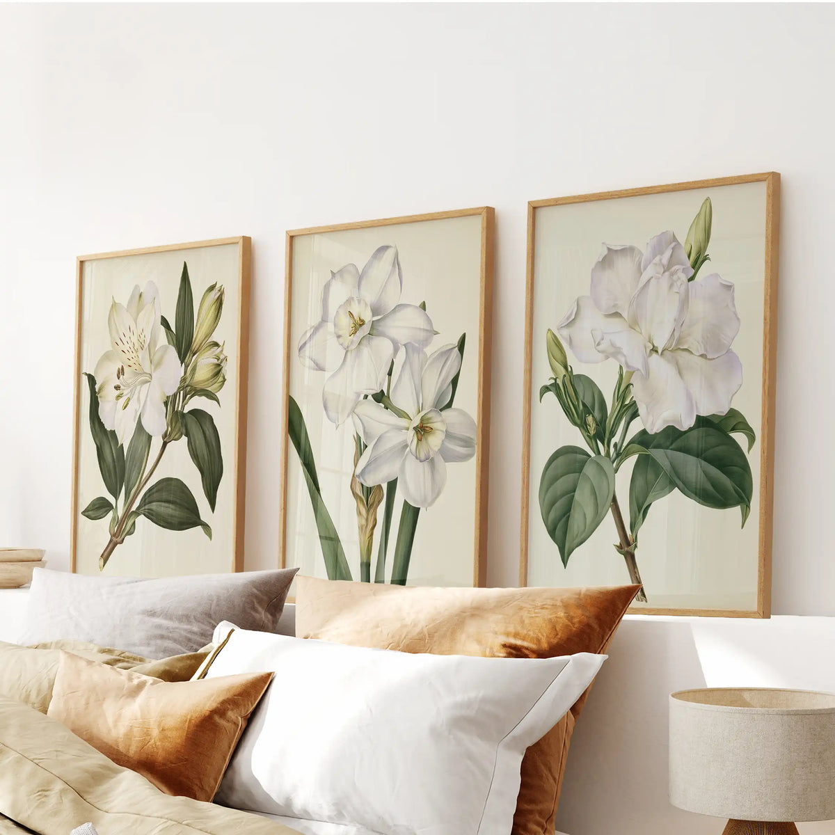 White flower and bud prints in oak frames, a set of three above a bed.