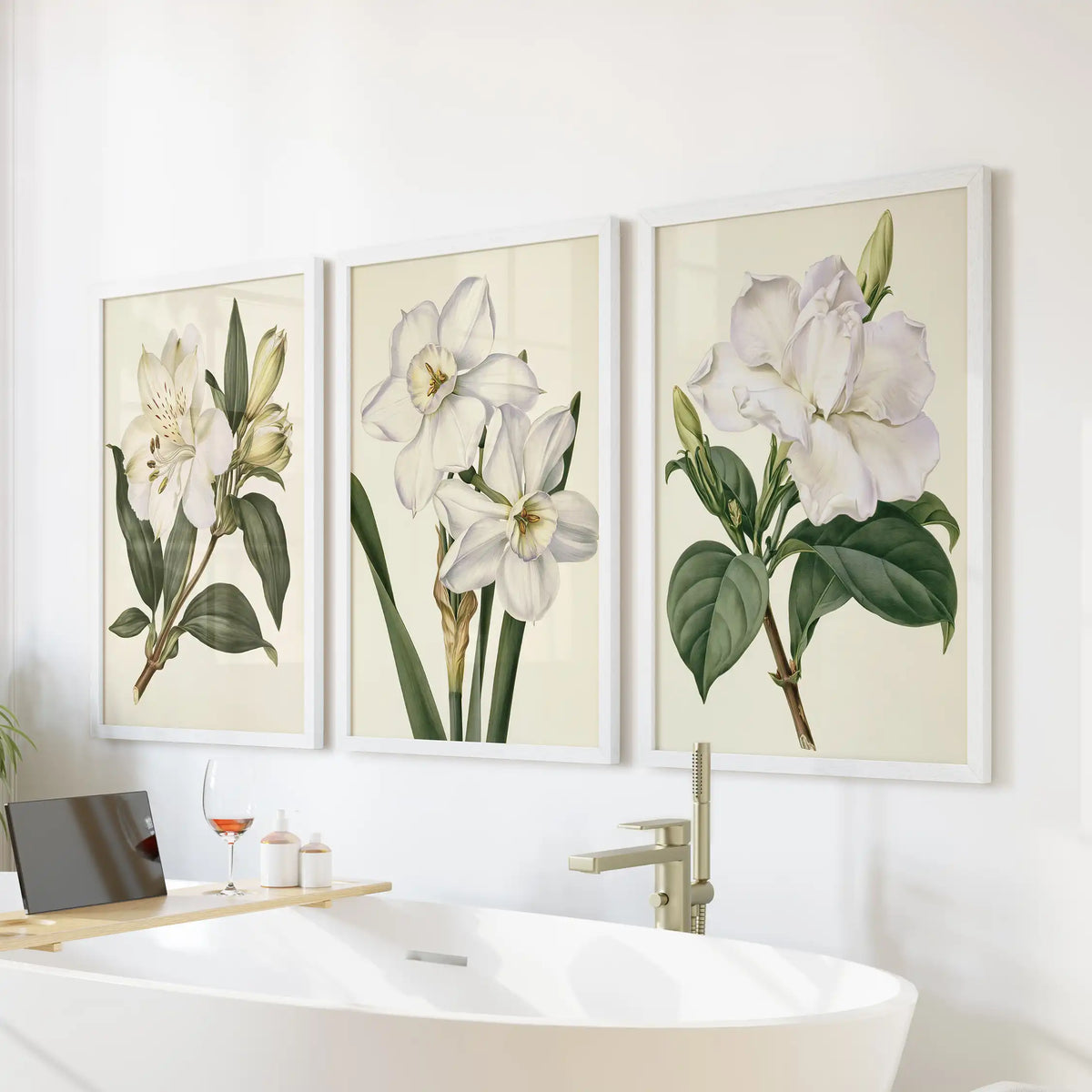 White flower and bud prints in white frames, a set of three above a freestanding bathtub.