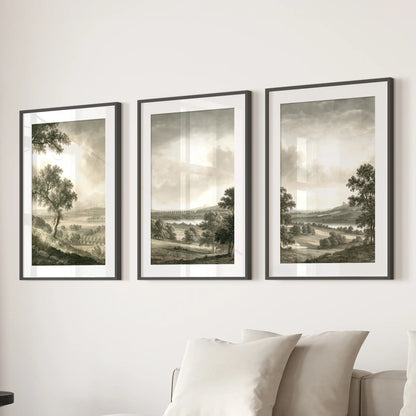 Rural landscape wall decor in three pieces, shown in black frames with white mats above a sectional sofa in a lounge.