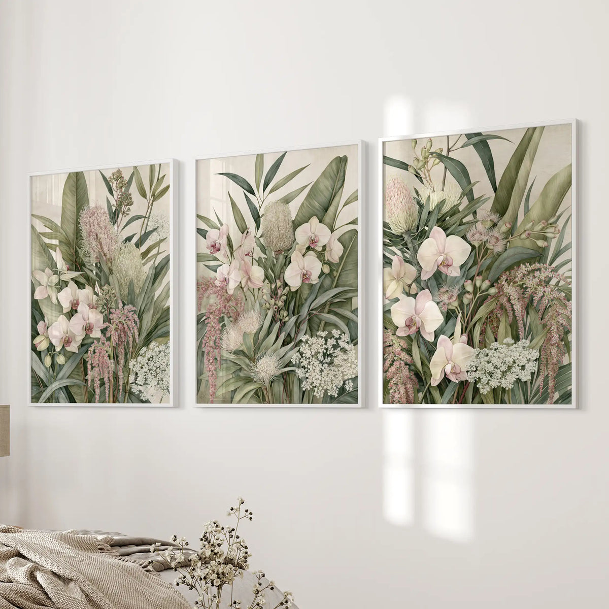 Pink orchids and tropical leaves fill three white-framed prints beside a bed.
