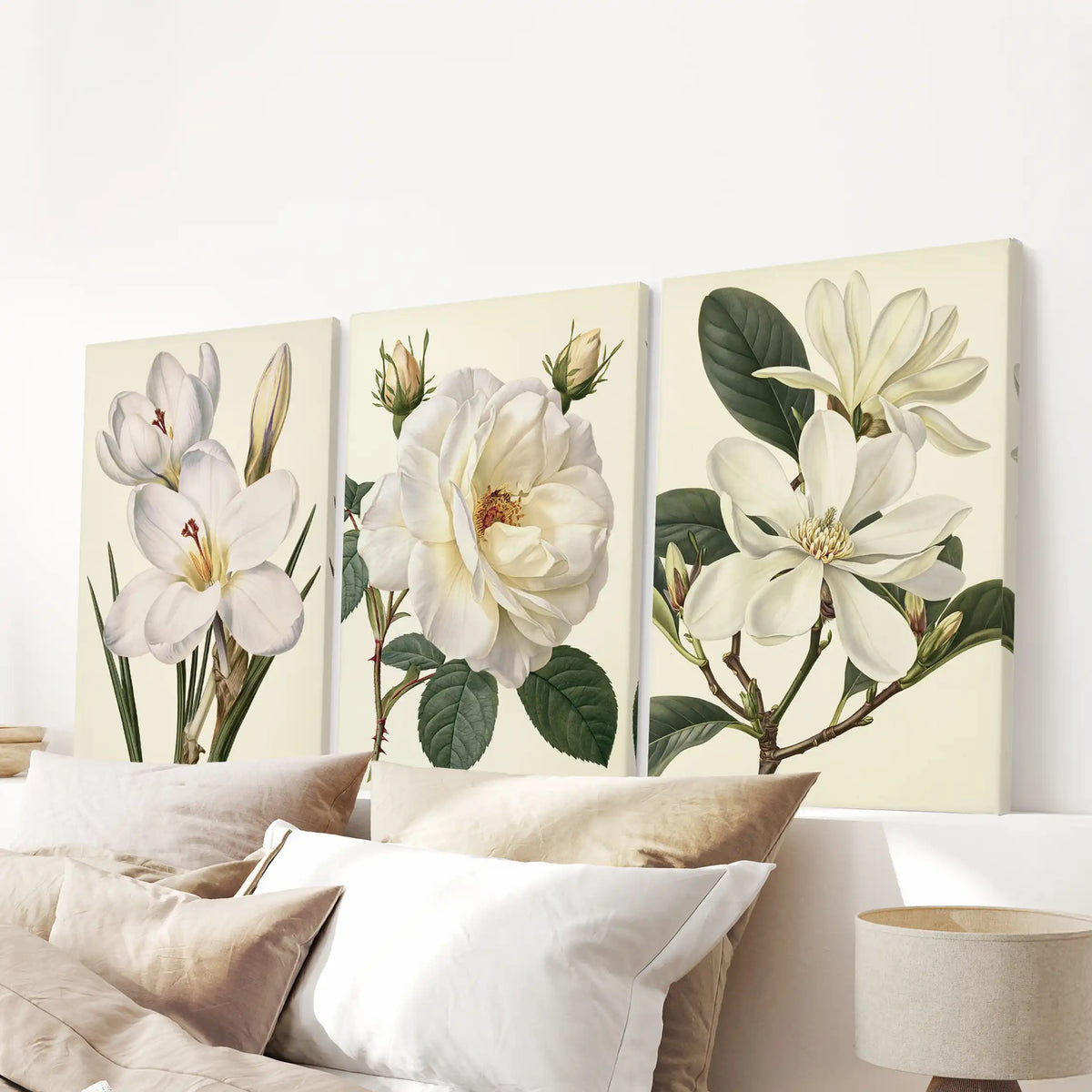 White petals and green leaves stand against cream backgrounds on three canvases above a bed, with a rose and buds in the middle.