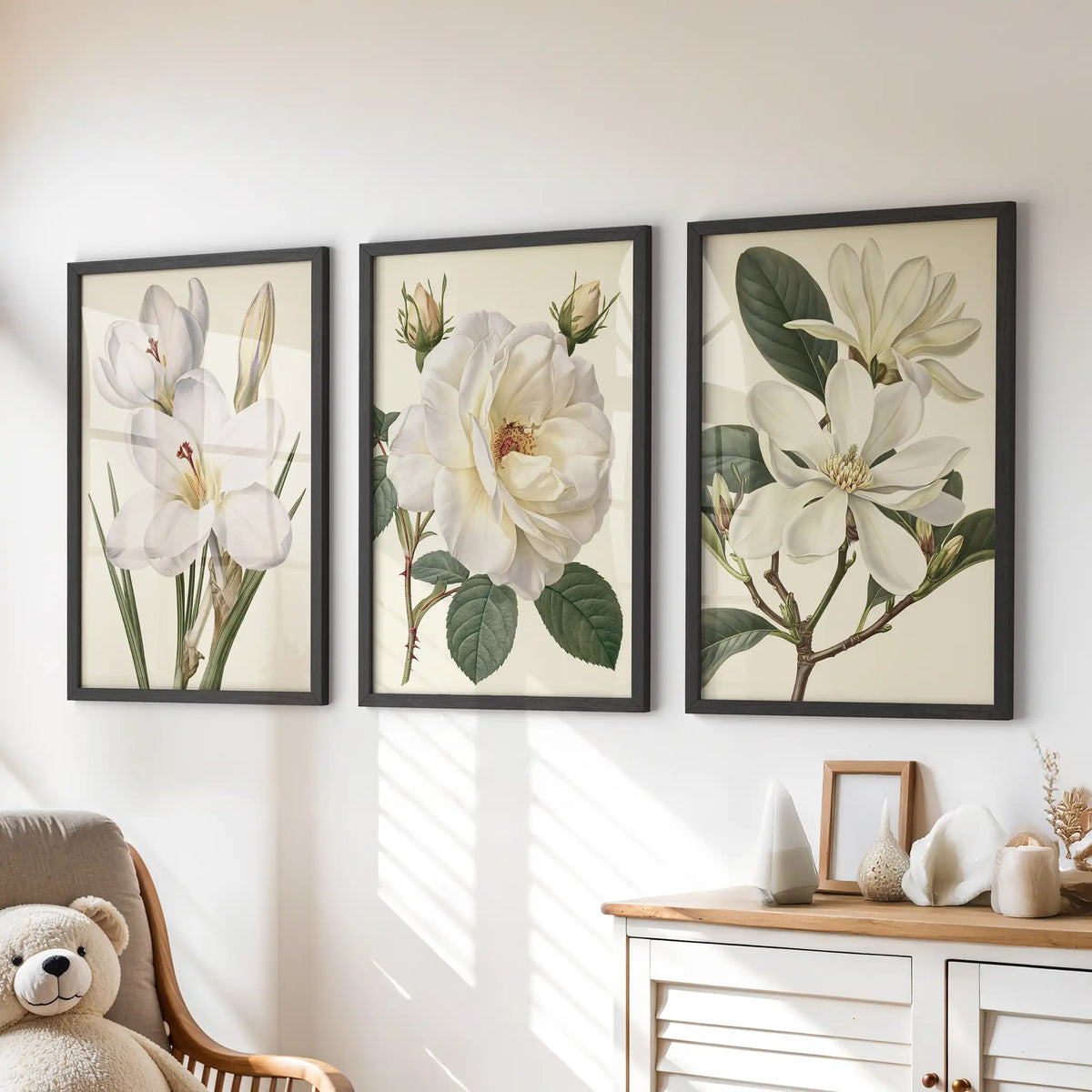 Above a dresser in a kids' room, black frames surround three prints of white petals and green leaves on cream backgrounds.