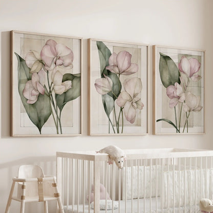 The three oak-framed prints above a crib show pink blossoms, slender stems and green leaves layered over fine rectangular outlines on cream.