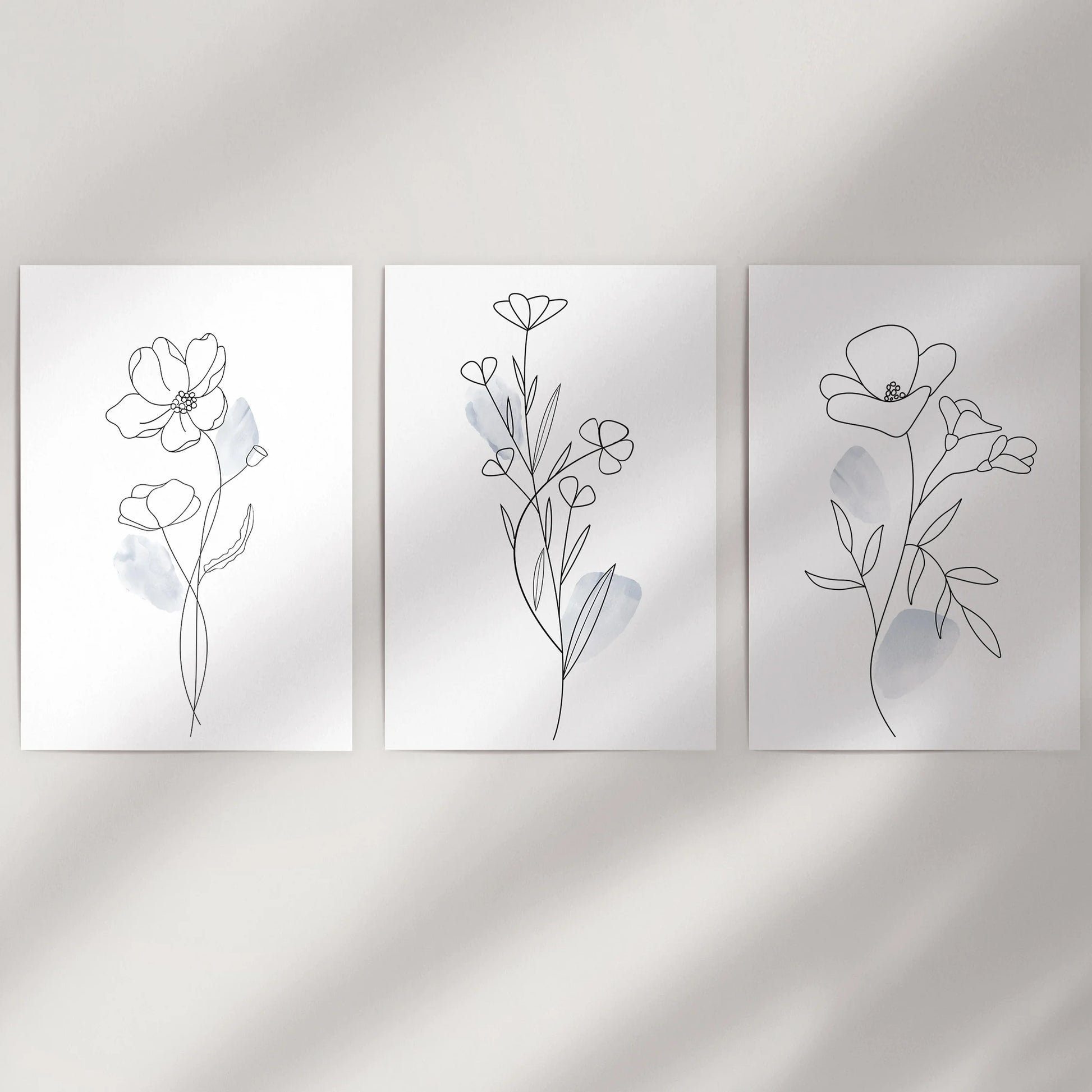 Three rolled wall art prints with abstract floral sketches hang lightly on a neutral wall, adding calm modern texture to the space.