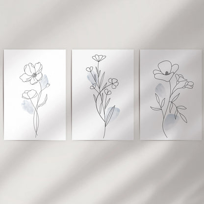 Three rolled wall art prints with abstract floral sketches hang lightly on a neutral wall, adding calm modern texture to the space.