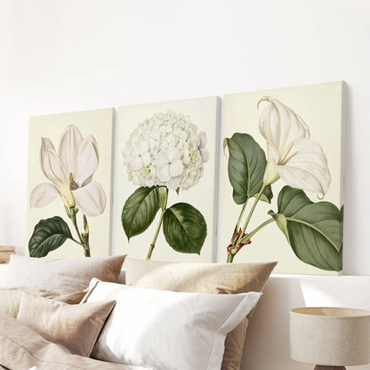 A set of three white flower and greenery canvases above a bed.