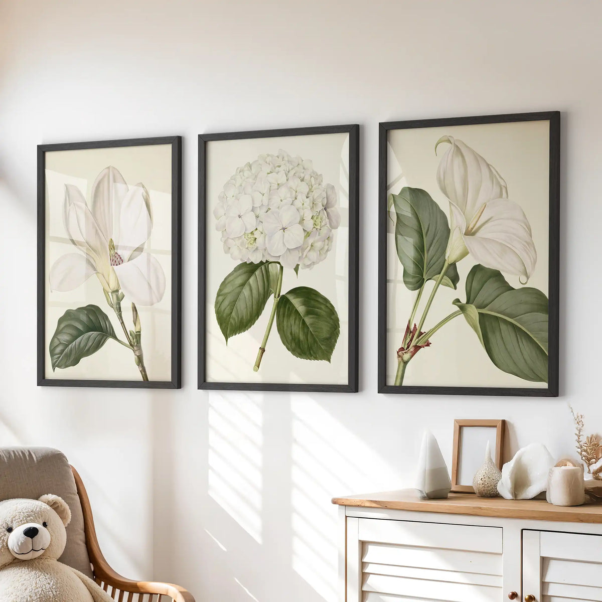 Above a dresser, three black-framed prints show a central white hydrangea, two larger white blooms and broad green leaves on cream.