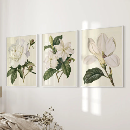 White flowers and green leaves fill three white-framed botanical prints beside a bed.