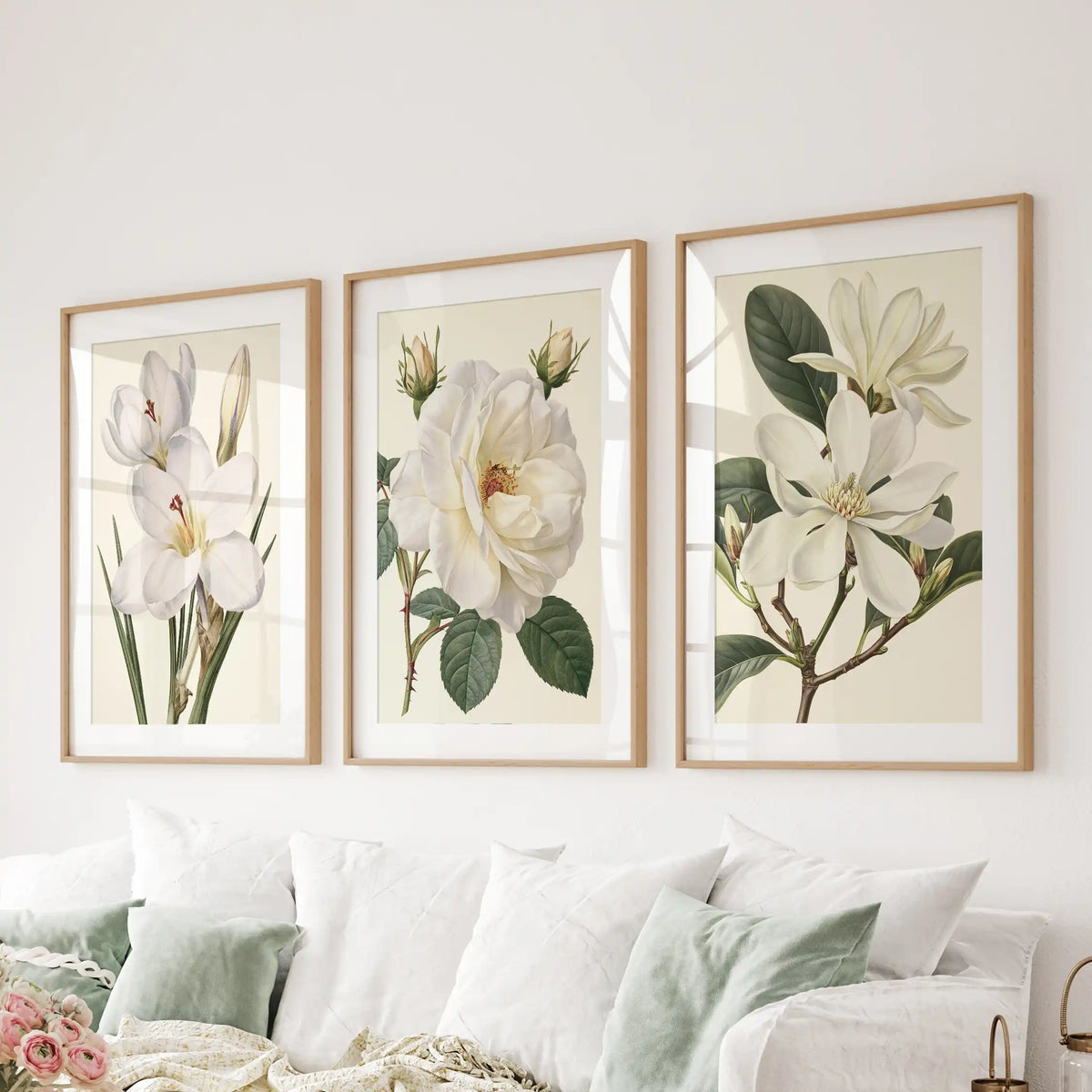 White mats surround the cream backgrounds of three flower prints above a sofa, with a rose and buds in the central oak frame.
