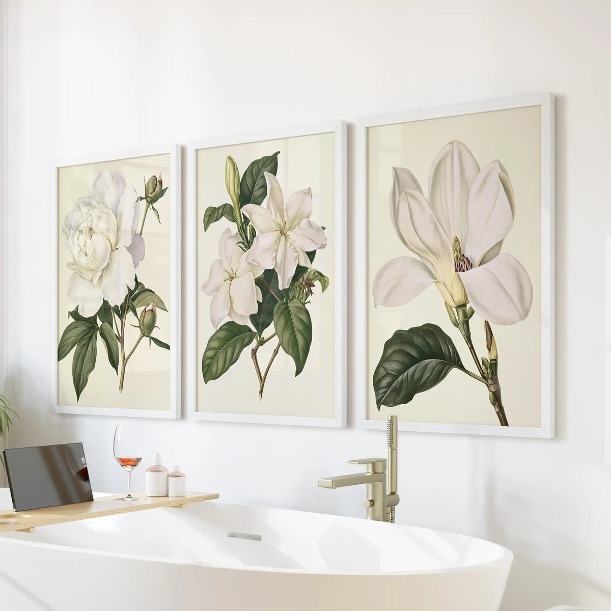 White petals and dark green leaves stand against cream in three framed prints above a bathtub, with a large ruffled bloom at left.