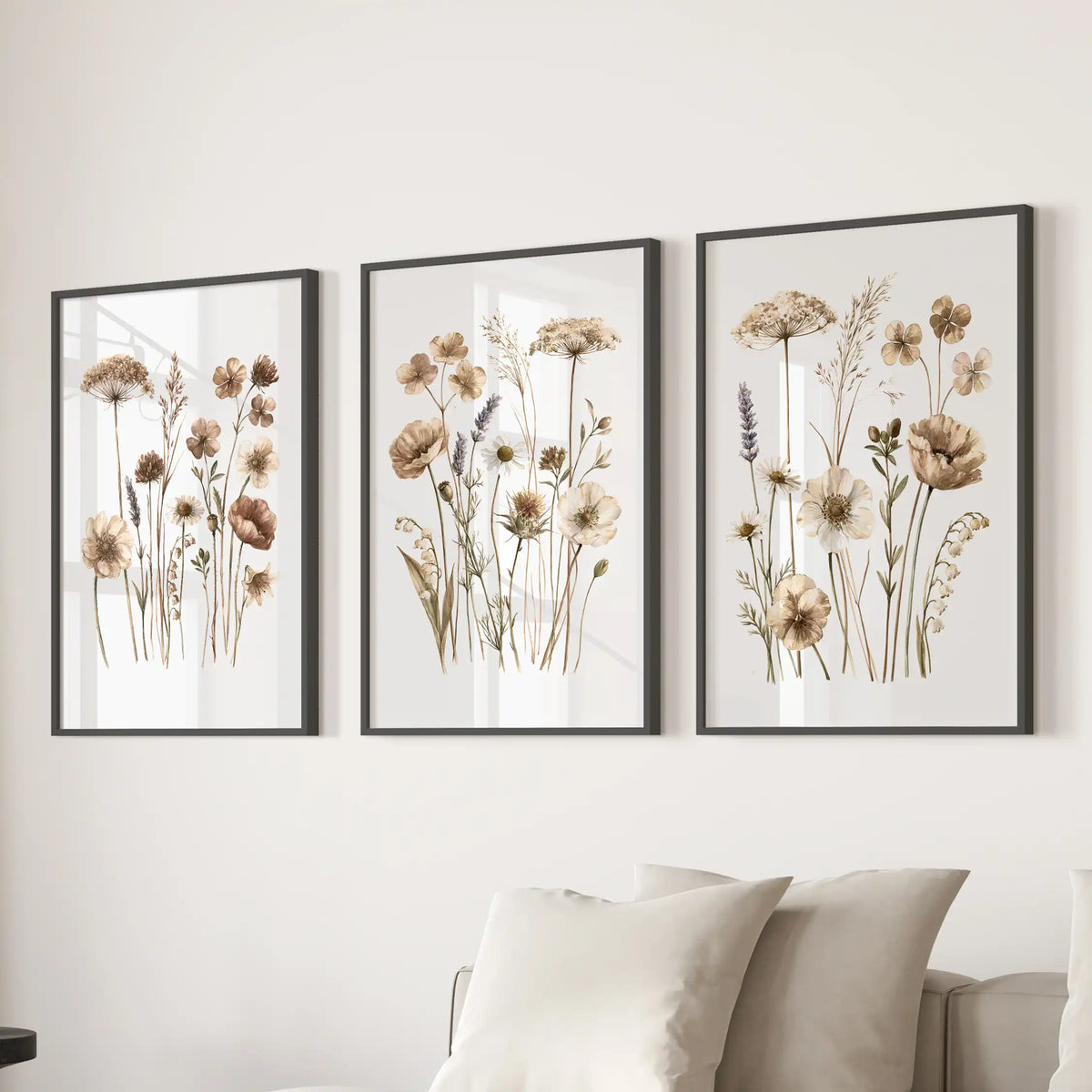 Beige meadow flower prints in black frames, a set of three above a sofa.